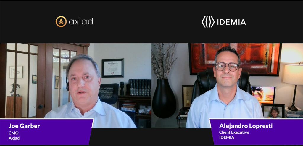 A picture of Axiad CMO Joe Garber talking with Alejandro Lopresti, IDEMIA